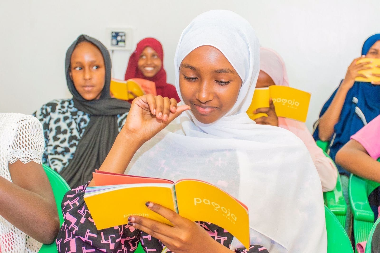 A girl smiles as she reads her Girls Book in a group session (Horn of Africa Institute · Nairobi · April 2024)