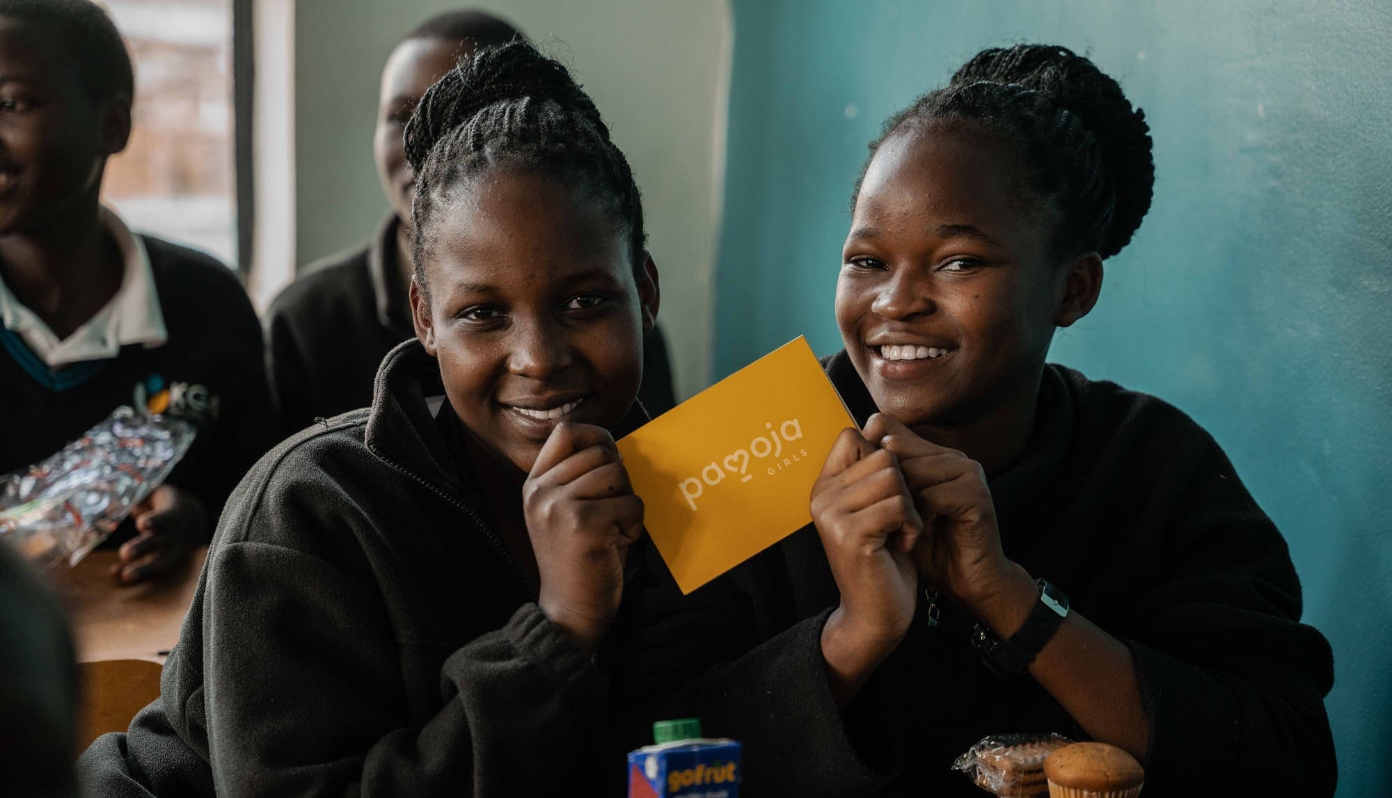 Two smiling girls hold a Pamoja Girls Book between them