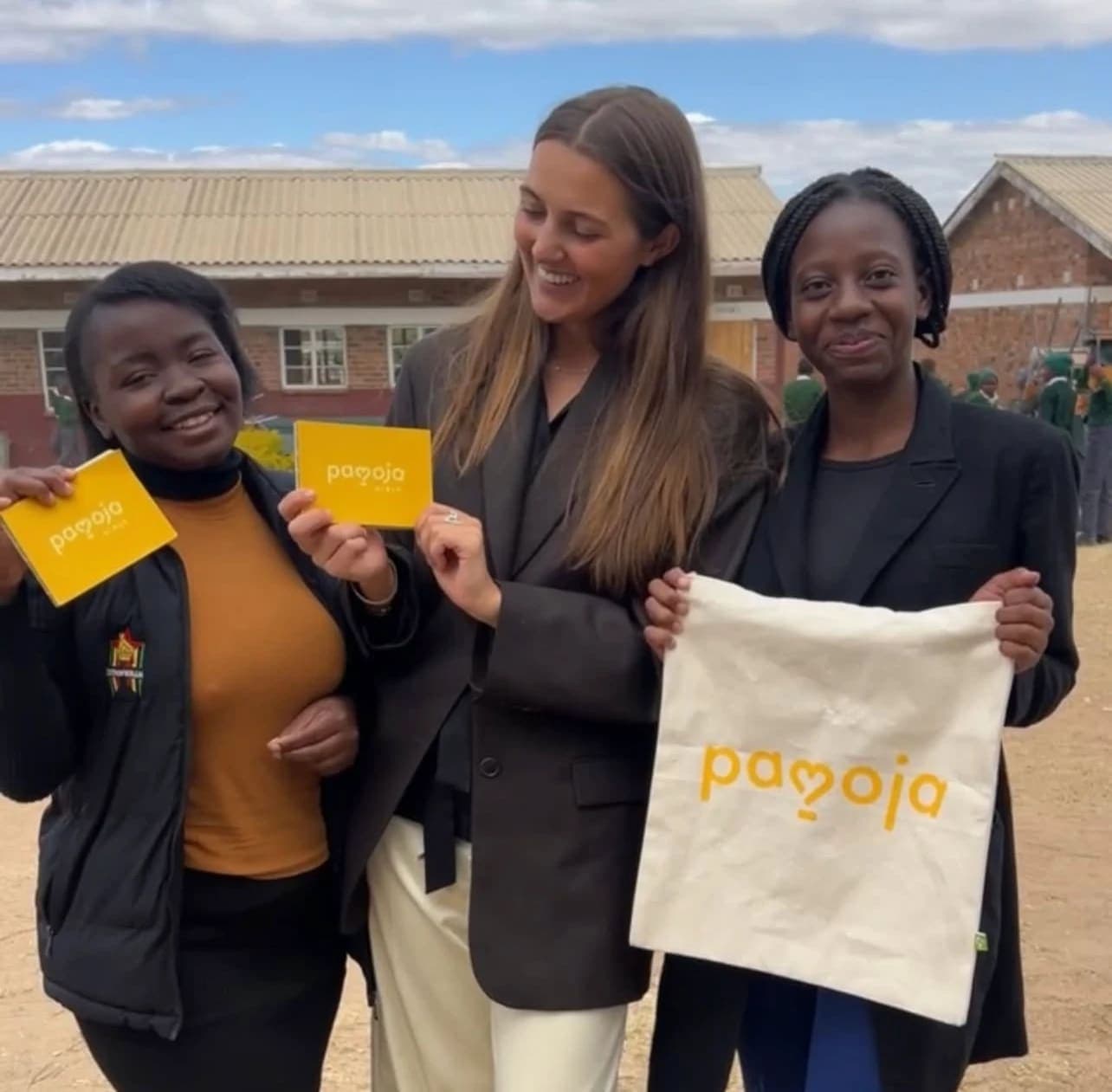 Pearl and Ethel from YASD with Amanda from the Pamoja Girls team, holding Pamoja Girls Books and a Pamoja Girls bag in the schoolyard (Young Achievement Sports for Development · Harare · June 2024)